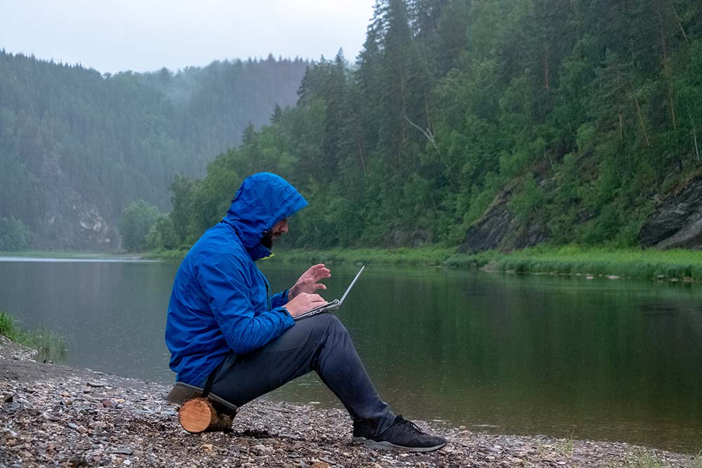 geospark–mining-exploration-solutions man sitting on log while on laptop in front of lake